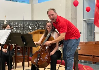 Man shows mock surprise while holding smiling student's bow on student's cello
