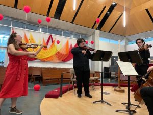 woman in orange dress plays violin with students