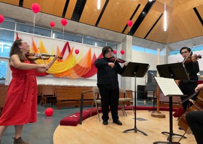 woman in orange dress plays violin with students