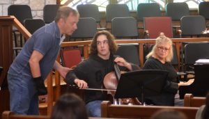 Man engages with student cellist as piano accompanist looks on