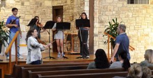 Man and woman instruct violin quartet on stage of a church