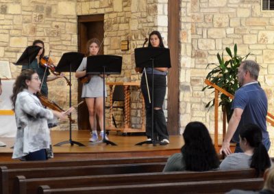 Man and woman instruct violin quartet on stage of a church