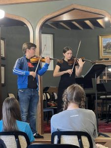 Teacher in foreground plays violin with student in background