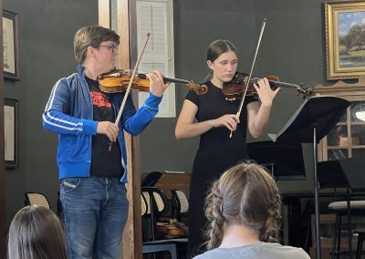 Teacher in foreground plays violin with student in background