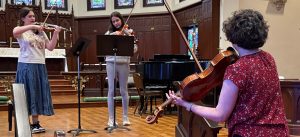 Teacher in foreground demonstrates on viola while students plays along