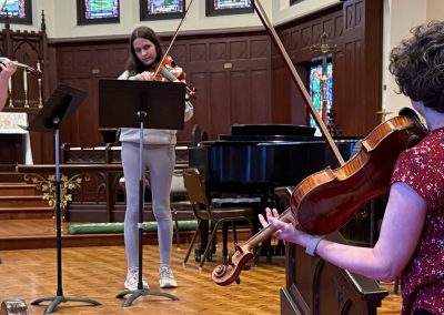 Teacher in foreground demonstrates on viola while students plays along