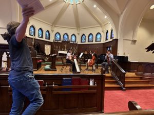 Teacher gesticulates with score in hand in the foreground while student quartet listens in the background
