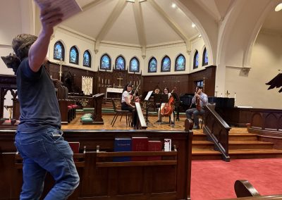 Teacher gesticulates with score in hand in the foreground while student quartet listens in the background